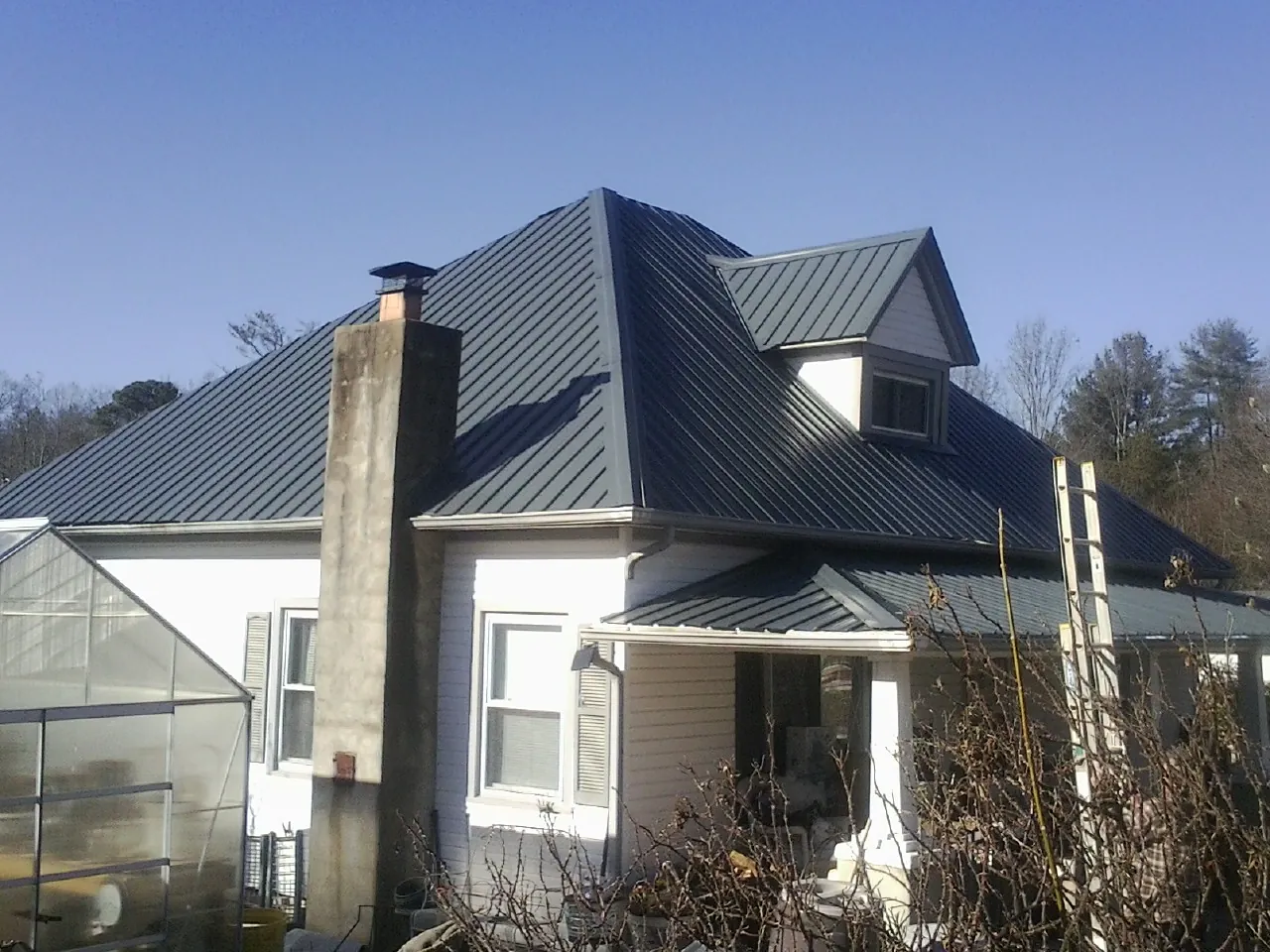 Dark blue standing seam metal roof on a white farmhouse with dormer — Slate & Tile Roof Repair by Roofing Brothers in Coopersburg