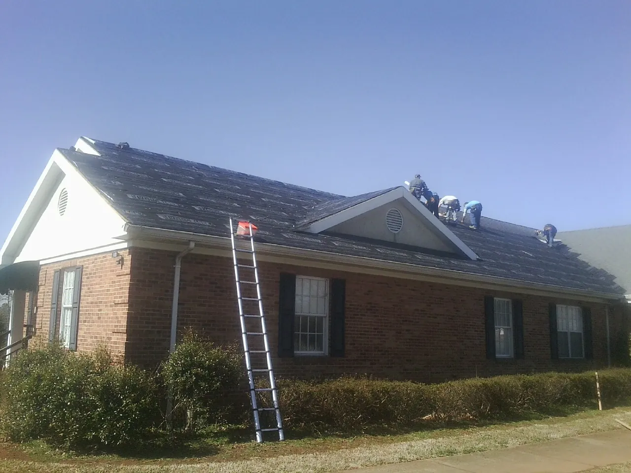 Crew tearing shingles off a brick ranch roof with a ladder set — Emergency Roof Repair work by our crew in Coopersburg