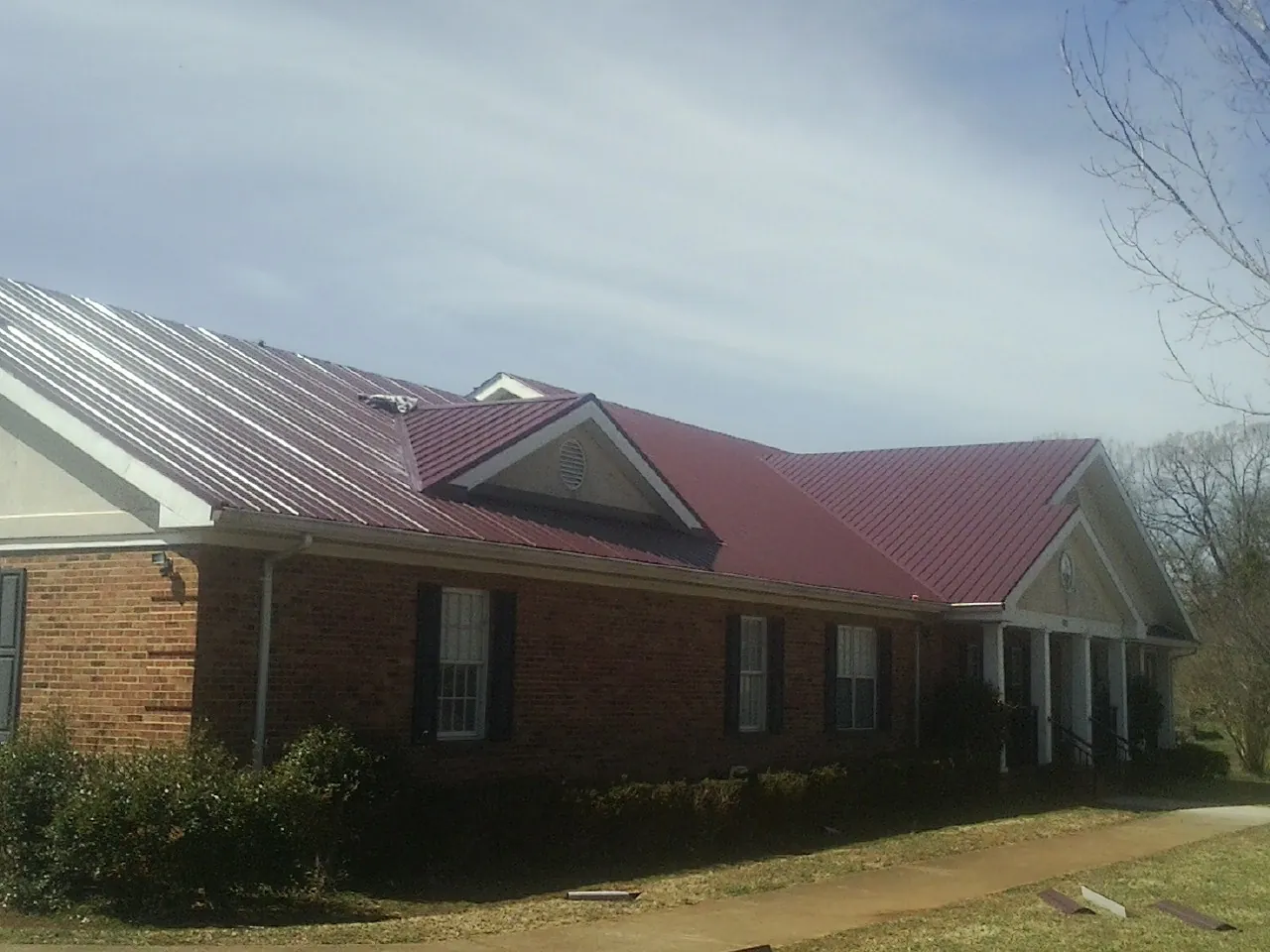 Red metal roof with gabled entries on a long brick building, from a Hail Damage Roof Repair job in Coopersburg