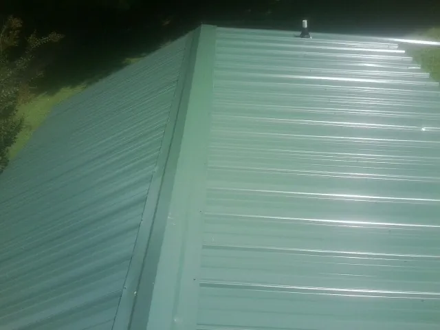 New green metal panels meeting at the ridge of a roof — Flat Roof Repair work by our crew in Coopersburg