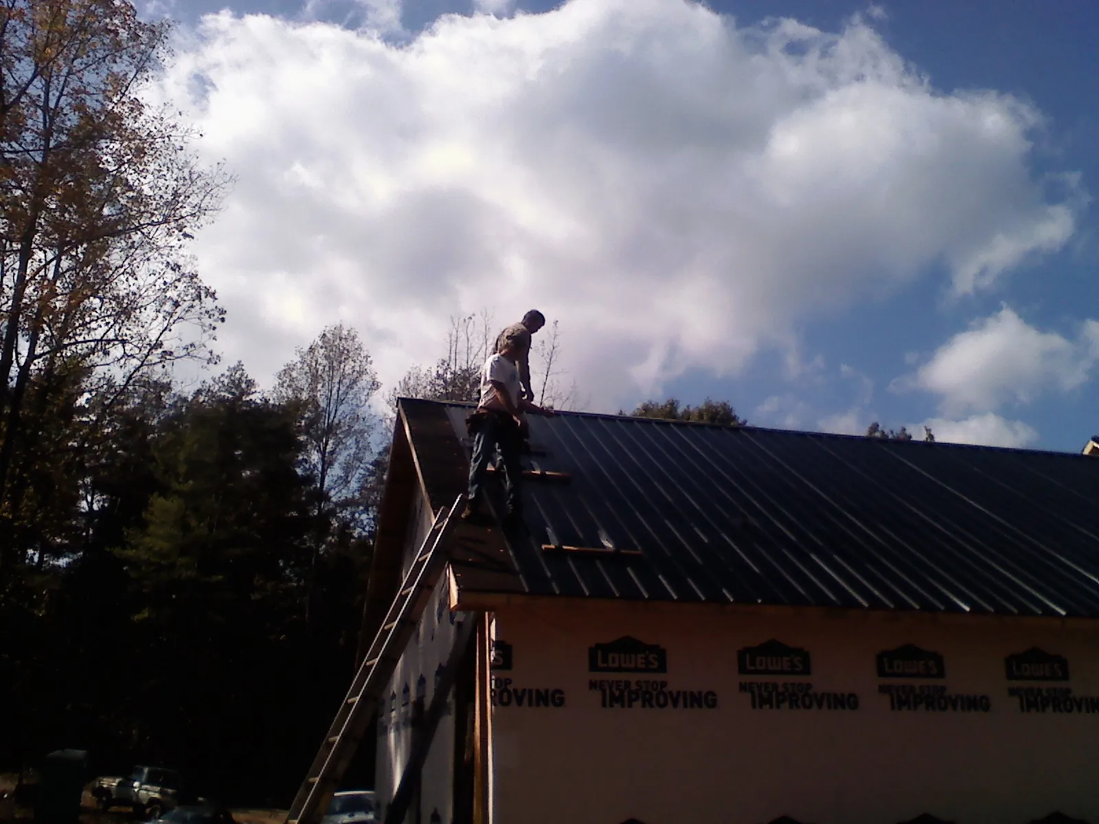Roofer fastening dark metal panels high against a cloudy sky, from a Roof Inspection job in Coopersburg