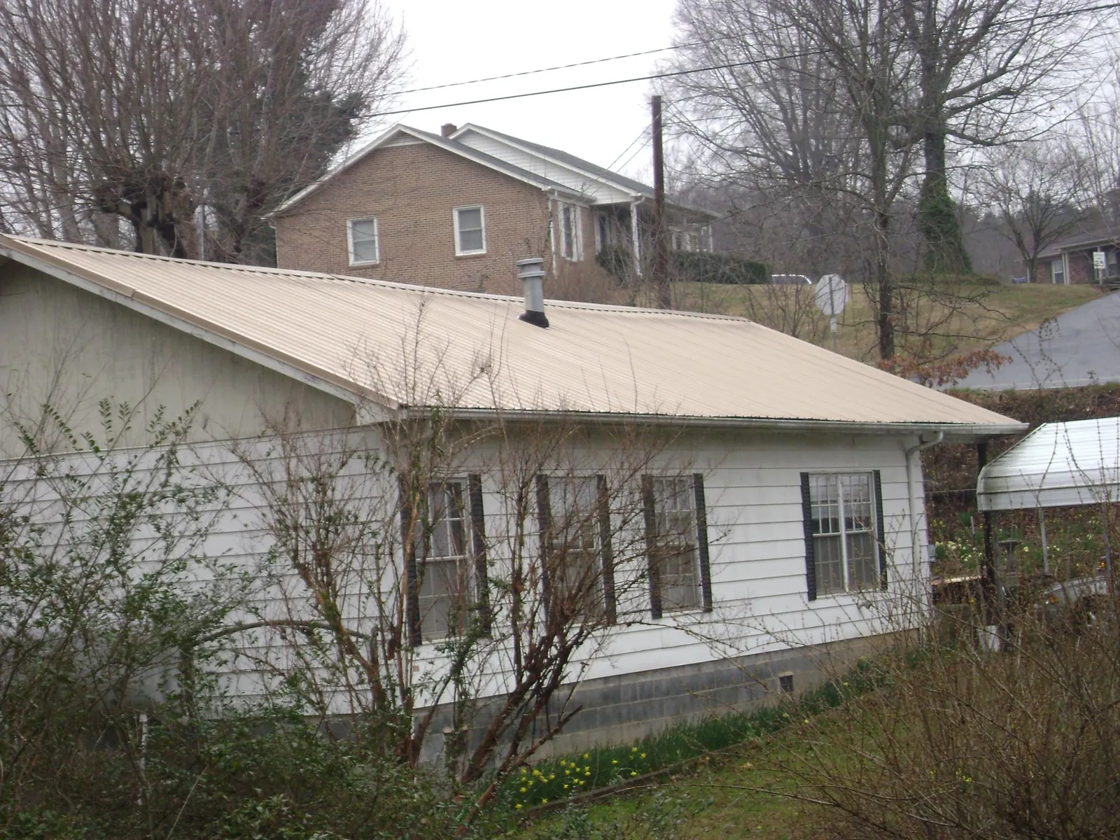 Tan metal roof on a white sided house set into a hillside — Commercial Roofing by Roofing Brothers in Coopersburg
